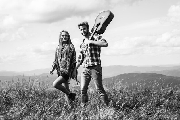 Una donna sorridente allegra e un uomo hipster con la chitarra si divertono in montagna