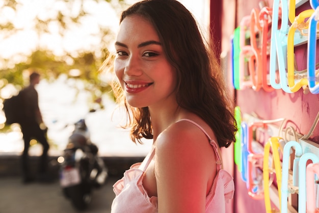  a cheerful smiling young pretty woman at the beach party near bright led colorful wall in cafe bar.