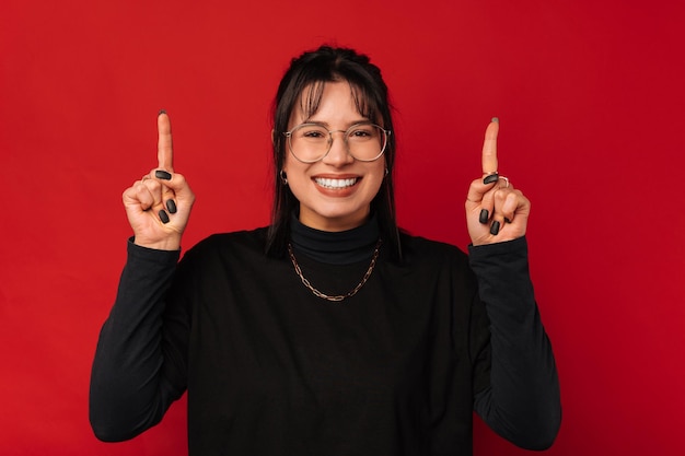 Cheerful smiling young woman is pointing up above her head with both hands