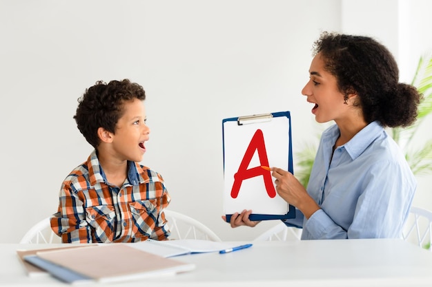 Photo cheerful speech therapist curing boys problems showing a letter indoor