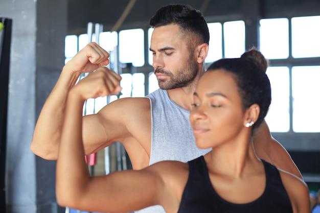 Cheerful sportive couple training together and showing biceps at the gym.