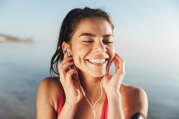 Cheerful sports woman listening music in earphones with closed eyes