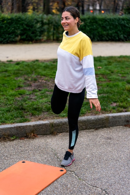 Cheerful sportswoman stretching leg in park