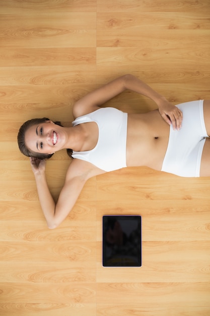 Cheerful sporty brunette lying next to a tablet