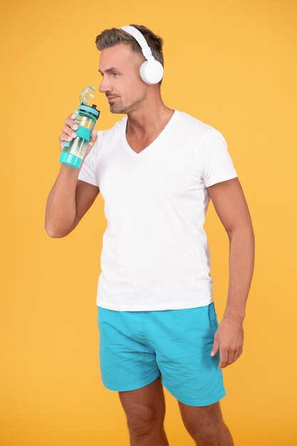 ヘッドフォンで陽気なスポーティな男は水を飲みます スポーティな男は黄色に分離された水を飲みます