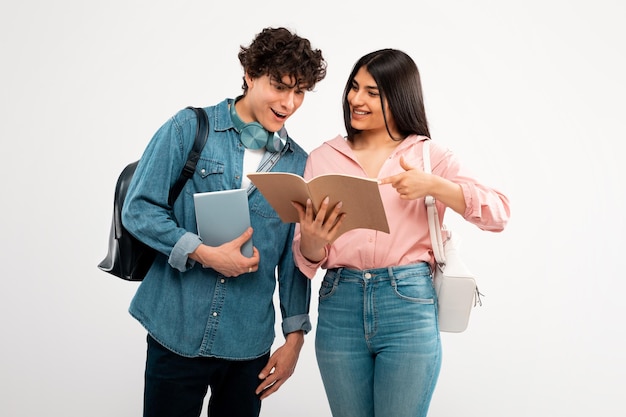 Cheerful student lady showing workbook to guy over white background