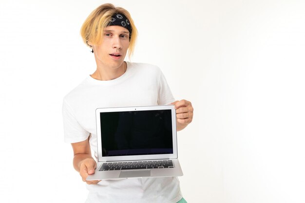 Cheerful student on a white  with a smile looks at the camera, holds a laptop in his hands with a blank screen on a white isolated 