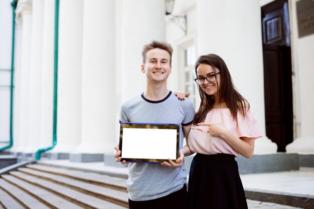 Cheerful students showing laptop with copy space and pointing to the screen