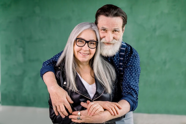 cheerful stylish bearded man embracing his gray haired wife from the back and looking at camera 