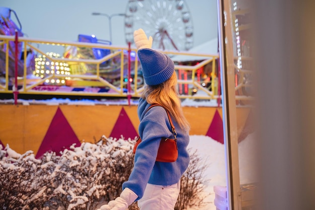 Cheerful and stylish woman dressed in warm clothes is having fun in a snowy winter amusement park