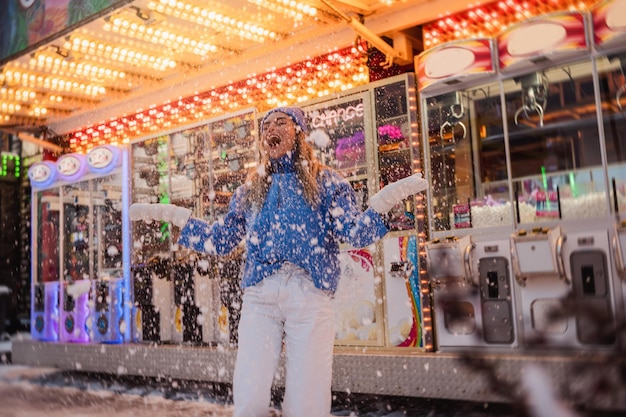 Photo cheerful and stylish woman dressed in warm clothes is having fun in a snowy winter amusement park