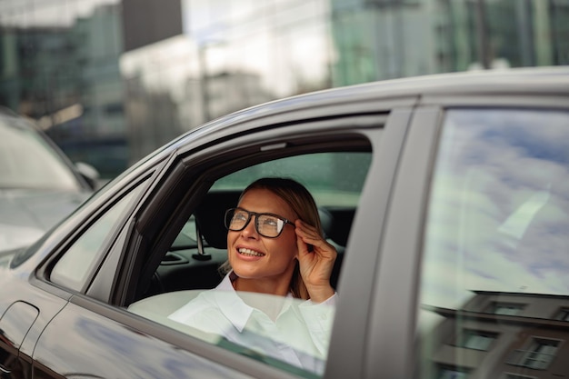 Веселая стильная женщина в очках, путешествующая на машине и смотрящая в окно