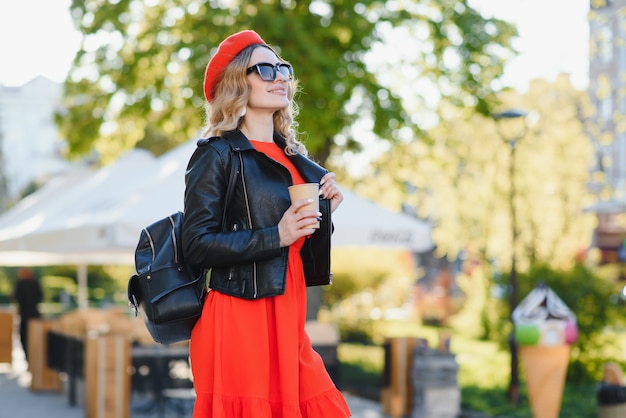 Giovane donna alla moda allegra in strada a bere il caffè del mattino nella luce del sole.