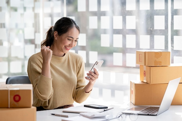 Allegro successo donna asiatica la sua mano alza la scatola di imballaggio per il marketing online e il concetto di idea per le pmi di consegna