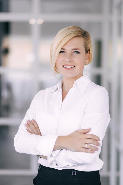 Cheerful successful businessman posing against the background of the office Proud young woman in an office suit standing with crossed arms and smiling at the camera Business success concept