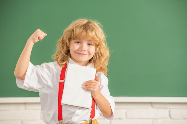 Cheerful successful kid boy in bow tie in school classrrom with book copy space education