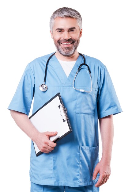 Cheerful surgeon. Cheerful mature doctor looking at camera and smiling while holding clipboard and standing isolated on white