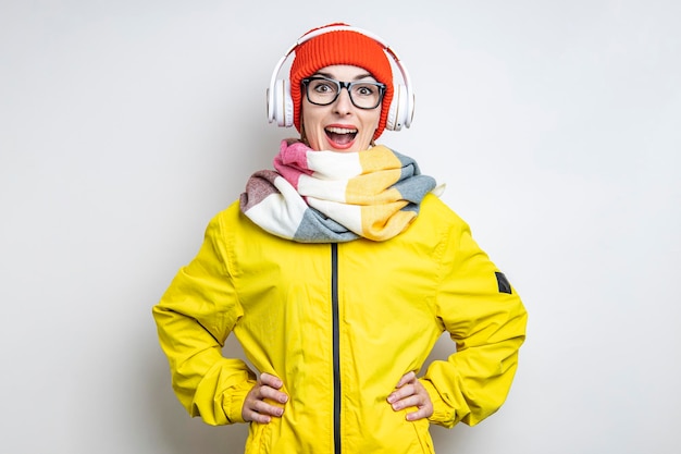 Cheerful surprised young girl in headphones in a yellow jacket on a light background