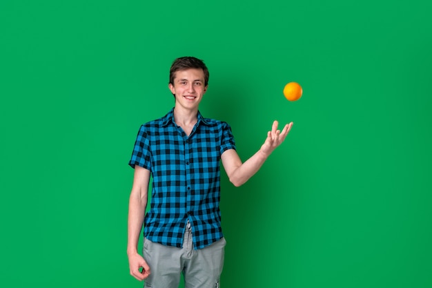 Cheerful tall Caucasian teenager holds an orange in his hand