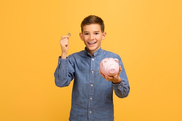 Cheerful teen boy holding coin and pink piggy bank