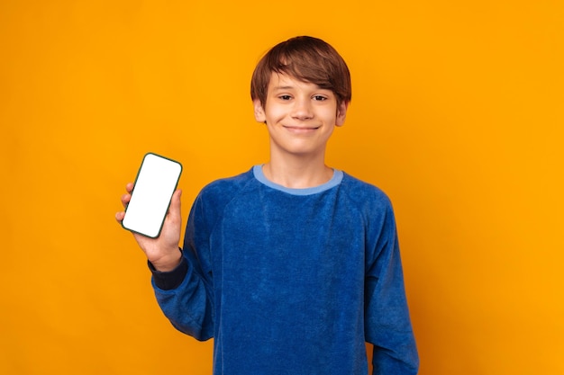 Cheerful teen boy is holding a phone with blank white screen with copy space