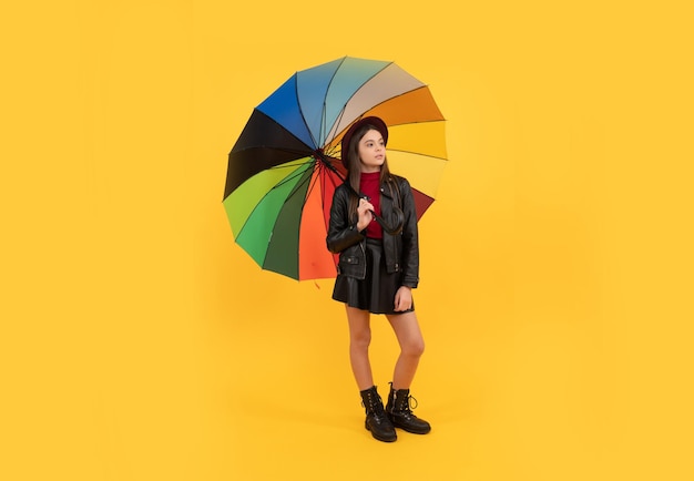 cheerful teen child hold colorful parasol. kid in hat with rainbow umbrella. autumn season. rainy weather forecast. back to school. fall fashion accessory. happy stylish girl in leather wear.