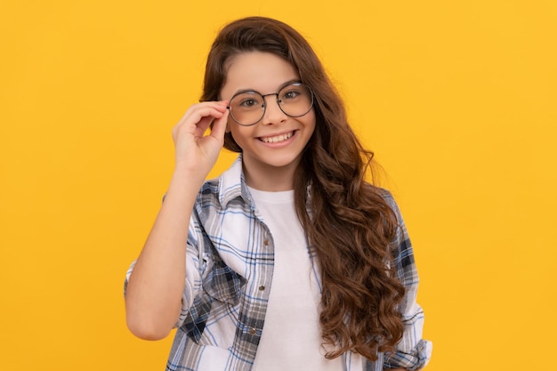 Cheerful teen girl in checkered shirt and glasses on yellow background