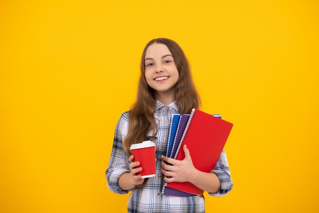 cheerful teen girl in checkered shirt holding coffee cup and notebook on yellow background, childhood.