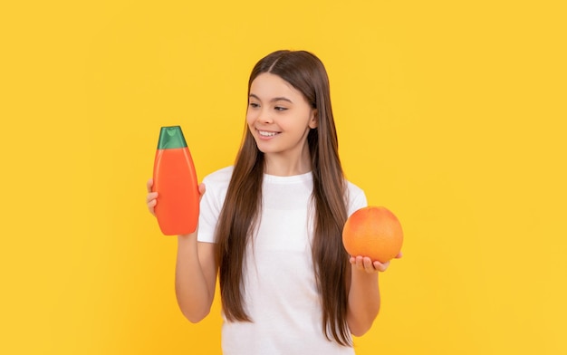 Cheerful teen girl long hair with body lotion and grapefruit on yellow background vitamin