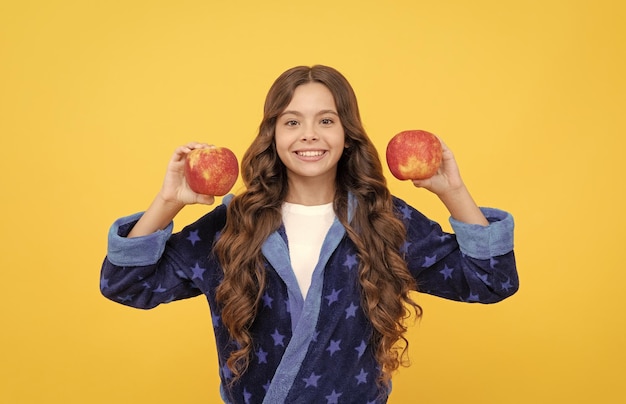 Cheerful teen girl with curly hair in comfortable pajama going to eat healthy apple vitamin