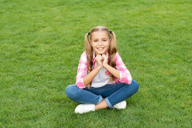 陽気な 10 代の子供が屋外の緑の芝生の上に座る