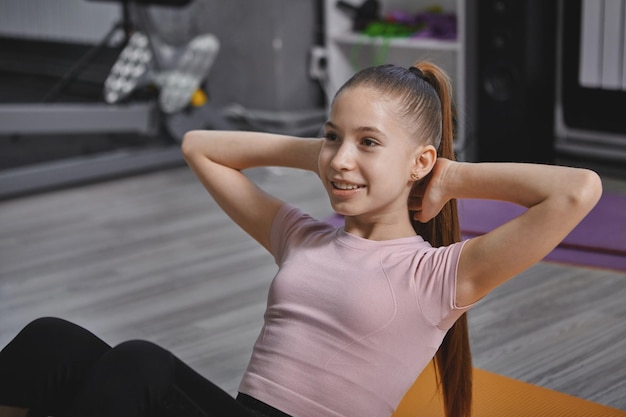 Photo cheerful teenage girl doing situps at the gym