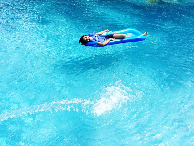 写真 プールでインフレータブル・ラフトに横たわっている陽気なティーンエイジャーの女の子