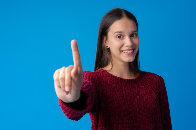 青い背景の上のカメラに指を指している陽気な10代の少女