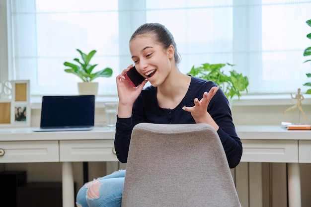 Cheerful teenage girl talking on phone at home