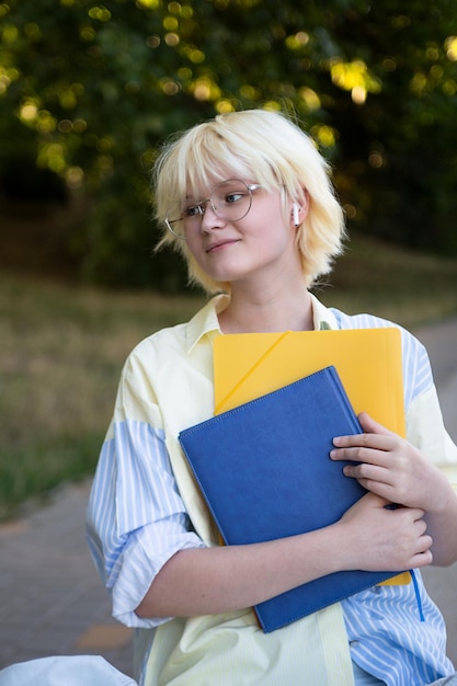 写真 黄色と青のフォルダとノートブックを手にした陽気なティーンエイジャーの女の子垂直写真