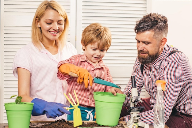 Фото Веселые три человека с милым ребенком выращивают растение в горшке маленький милый мальчик помогает своим родителям счастливая семья сажает росток в горшок