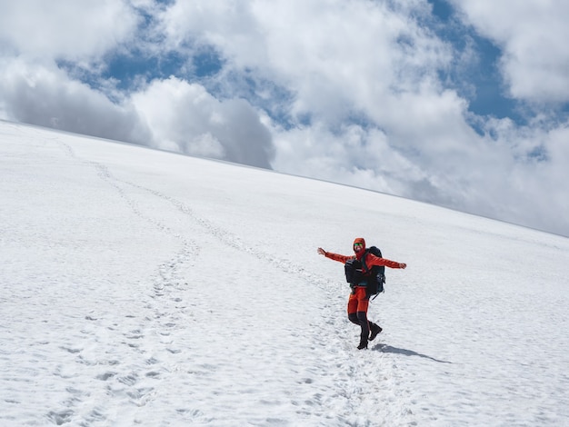 Cheerful tourist is fooling around on a glacier.Tourist hiking up the glacier. Winter hiking in the snow-capped mountains. Extreme recreation and mountain tourism.