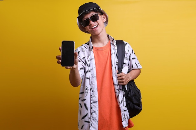 Cheerful tourist man showing blank screen empty smartphone mockup to camera while carrying backpack