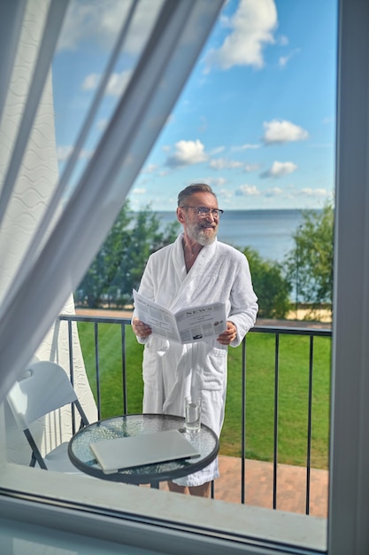 Cheerful vacationer with the open newspaper in his hands looking away