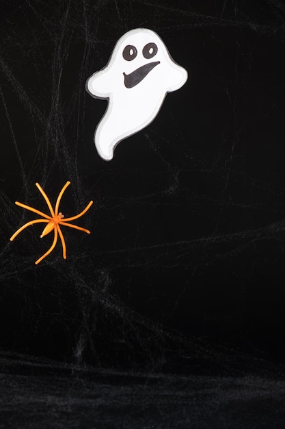 Photo a cheerful white ghost with a face smiles and flies on a black background with a web and spider