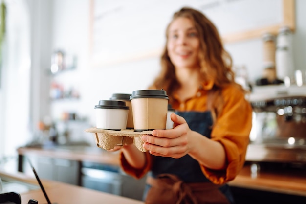 Foto donna allegra con un grembiule al bancone del bar che tiene bicchieri di caffè in un caffè concetto di cibo takeaway