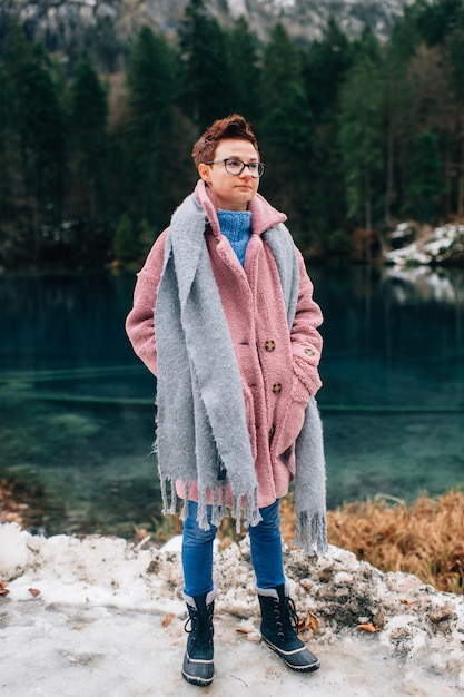 Cheerful woman in coat and long scarf standing near beautiful lake