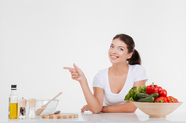 Cheerful woman cooking with vegetables while pointing left