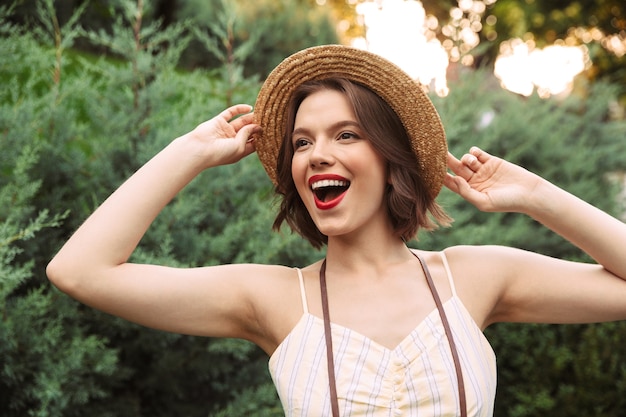 Cheerful woman in dress and straw hat having fun while looking away outdoors