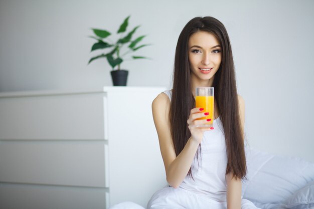 Cheerful woman drinking an orange juice sitting on her bed at home