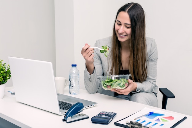 Жизнерадостная женщина ест салат в офисе