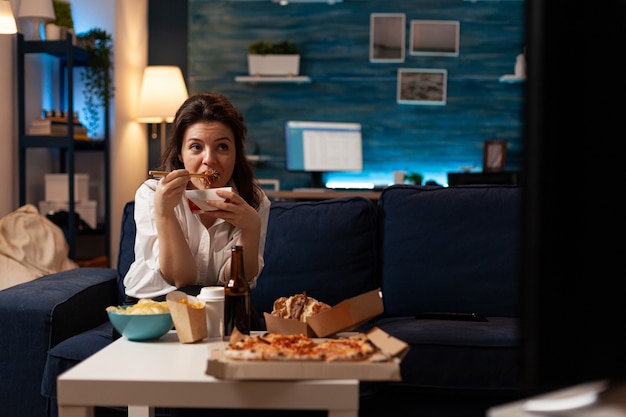 Cheerful woman eating tasty chinese food relaxing on couch