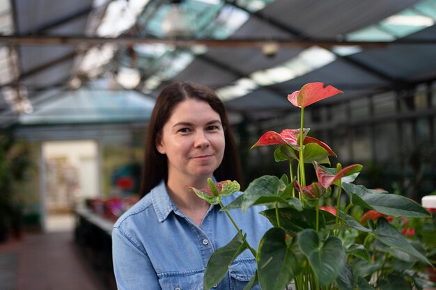 Cheerful woman in greenhouse with anthurium in the pot