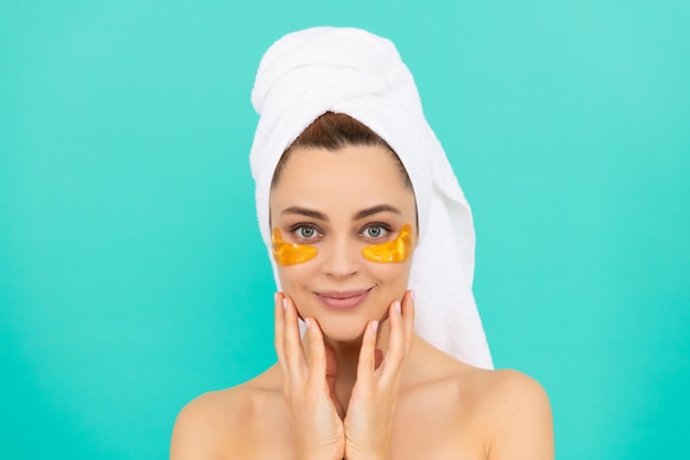 Cheerful woman has collagen golden eye patches on face with towel